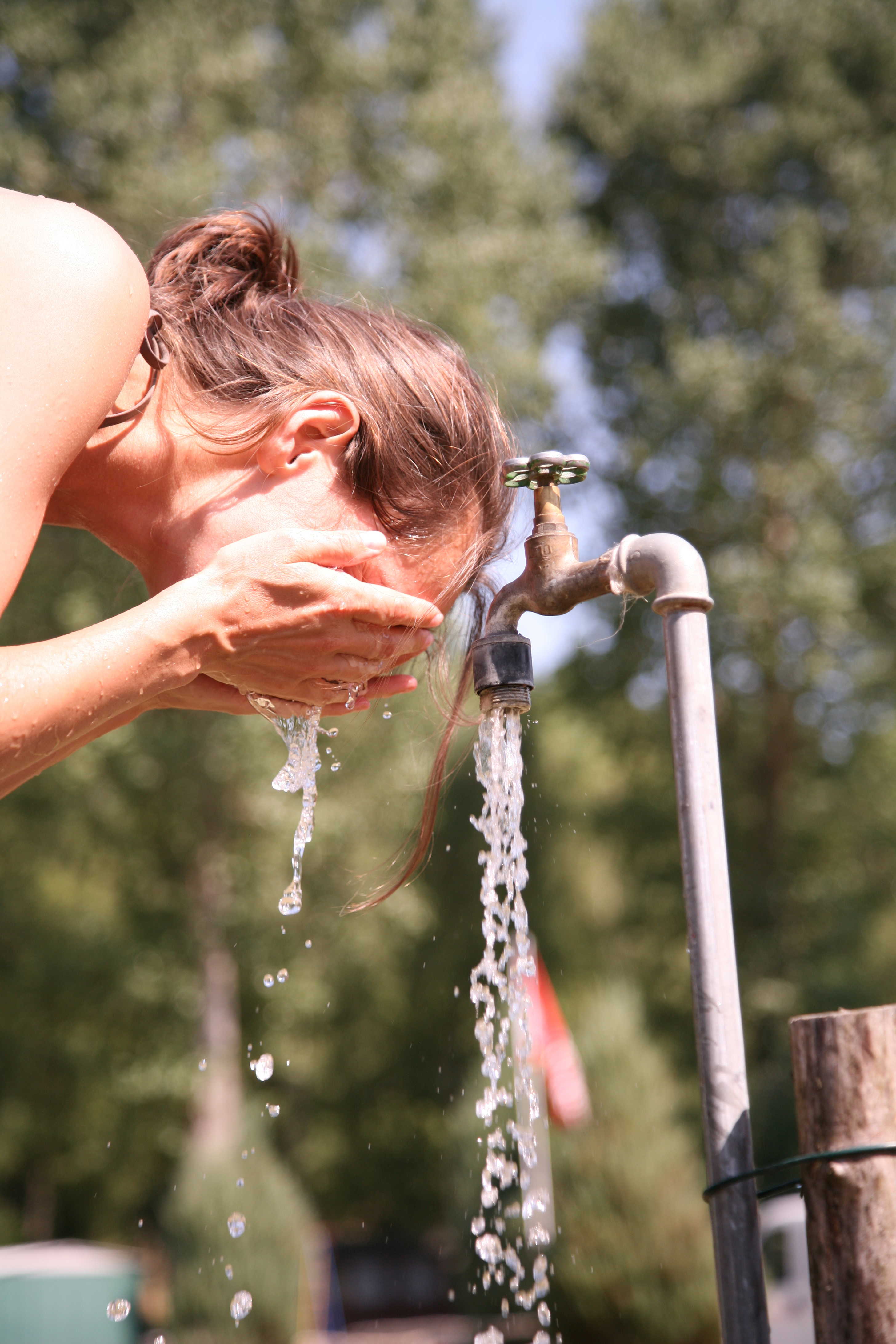 Kvinde vasker sig ansigt ved en udendørs vandhane