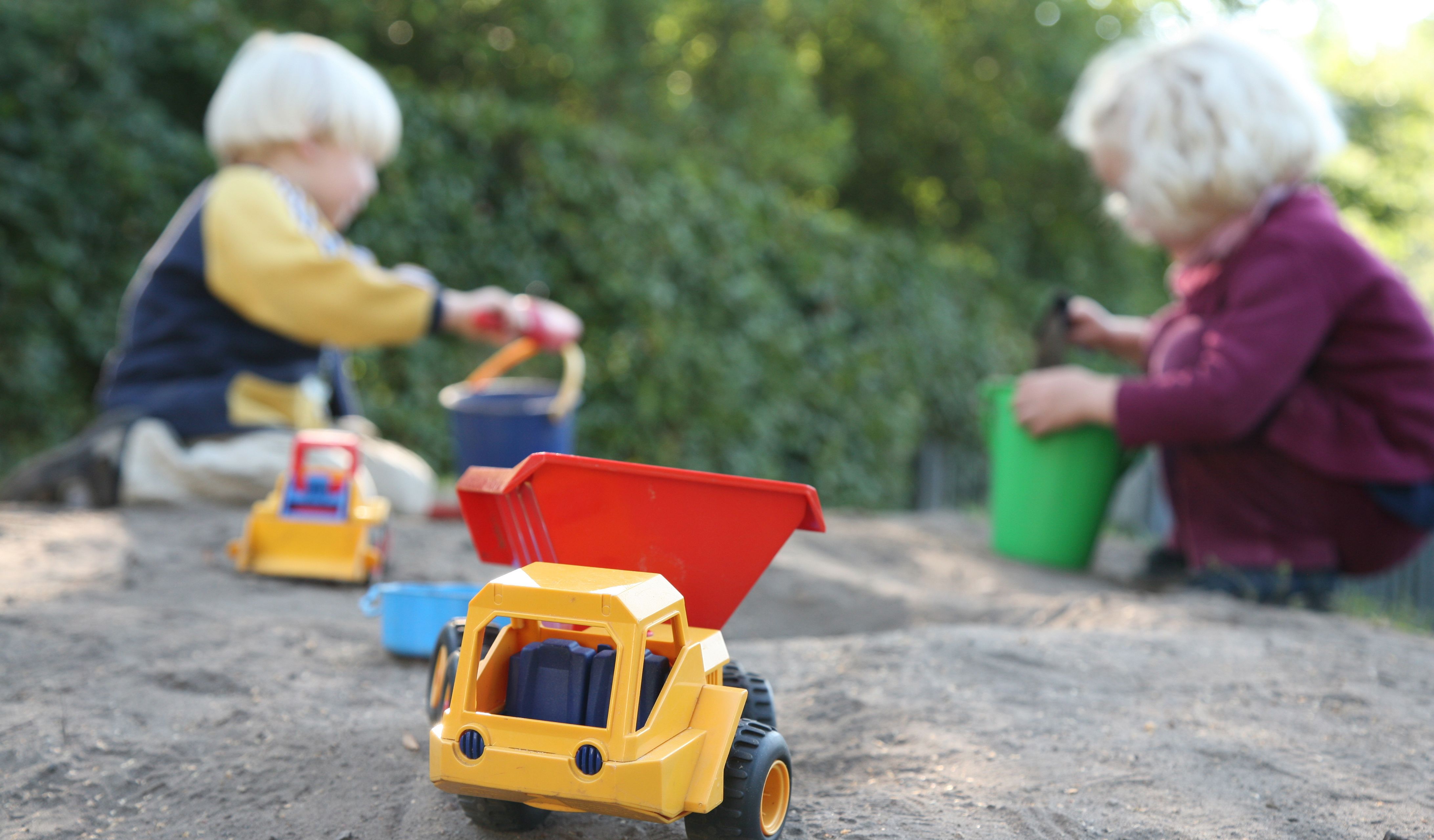 Børn, der leger i en sandkasse. Der er spande og skovle, og der er også små legetøjsbiler.