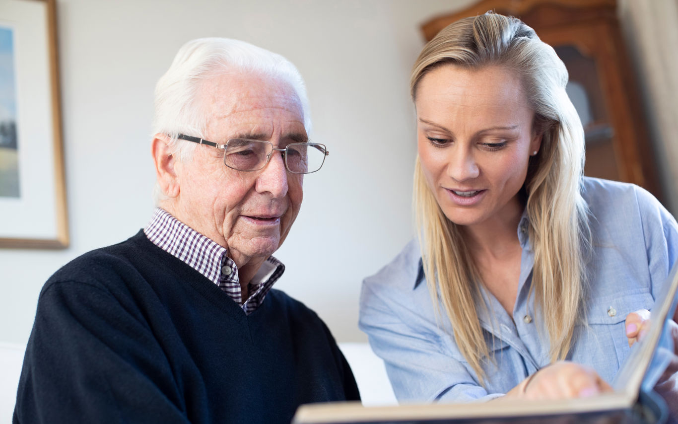 Ældre mand kigger på billeder med en lyshåret kvinde. Kvinden peger på et billede. Manden ser ud til at genkende det.
