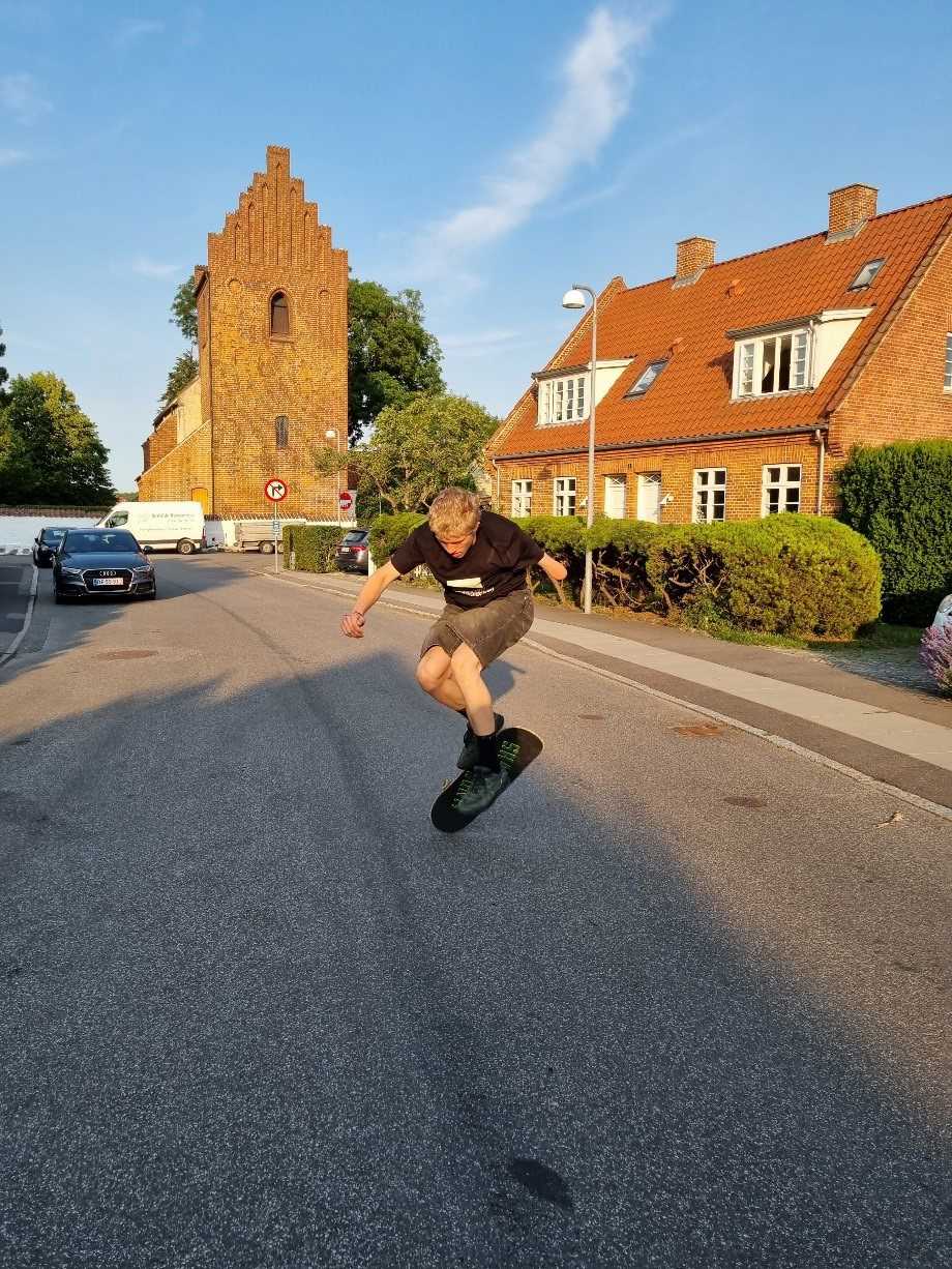Ung man, der skateboarder ned ad en asfalteret vej. Han er ved at lave et kick-flip.